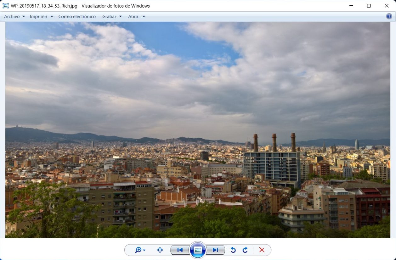 Ventana del Visualizador de fotos de Windows con una foto panorámica de una ciudad abierta, el menú Archivo, Imprimir, Correo electrónico, Grabar y Abrir arriba, y la barra de controles redonda abajo.